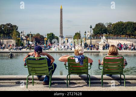 Drei Personen sitzen auf grünen Stühlen und blicken auf den Obelisken rund um den überfüllten zentralen Pool des Tuileries Gartens, Paris Frankreich Stockfoto