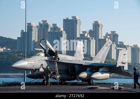 Busan, Südkorea. Oktober 2023. Die US-Navy-Matrosen führen routinemäßige Wartungsarbeiten an einem F/A-18E Super Hornet-Kampfflugzeug durch, das an der Royal Maces of Strike Fighter Squadron 27 befestigt ist, auf dem Flugdeck des Flugzeugträgers USS Ronald Reagan der Nimitz-Klasse bei der Abfahrt am 16. Oktober 2023 in Busan, Südkorea. Angabe: MC3 Heather McGee/USA Navy Photo/Alamy Live News Stockfoto