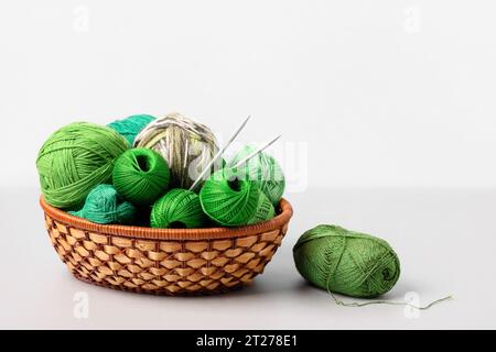 Grüne Strickbälle in einem Korb mit Stricknadeln auf grauem Hintergrund. Set für das Hobbys, warme Kleidung oder Spielzeug zu stricken. Konzeptnadelarbeit Stockfoto