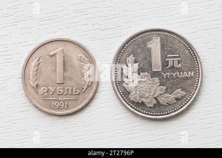 1 chinesische Yuan-Münze. Ein russischer Rubel. Zwei weiße Münzen liegen auf weißem Hintergrund. Stockfoto