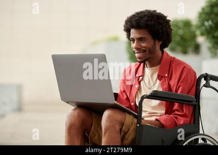 Lächelnder Schwarzer mit Behinderung, der am Laptop arbeitet Stockfoto
