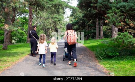 Mütter und Kinder gehen mit Kinderwagen auf einem von großen Kiefern gesäumten Weg im Royal Botanic Gardens Kew im Sommer 2023 London UK Stockfoto