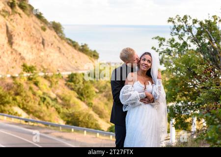 Frisch vermähltes Paar umarmt vor dem Hintergrund einer wunderschönen Berglandschaft, küsst der Kerl das Mädchen Stockfoto