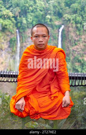 Bolaven Plateau, Südlaos, 17. Februar 2023: Gekleidet in traditionellen orangen Gewändern, typisch für asiatische Mönche. Der junge Mann sitzt auf einem Sicherheitsnetz. Stockfoto