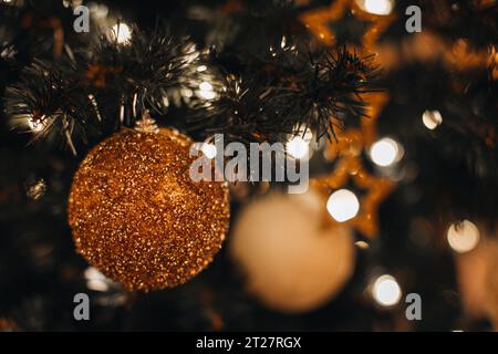 Details der Weihnachtskugel mit goldenem Glitzer, die an den Tannenzweigen hängen. Lichterbeleuchtung für die Winterferien Stockfoto