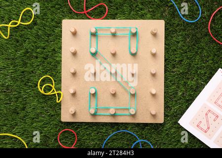 Geoboard aus Holz mit dem Buchstaben S aus Gummibändern auf Kunstrasen, flach gelegt. Lernspielzeug für die motorische Entwicklung Stockfoto