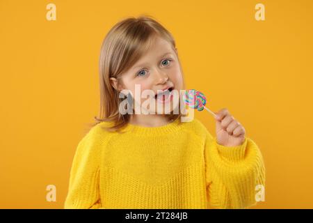 Porträt eines süßen kleinen Mädchens mit Lutscher auf orangefarbenem Hintergrund Stockfoto