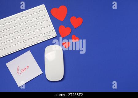 Fernbeziehung-Konzept. Computermaus, Tastatur, Liebesnotiz und Papierherzen auf blauem Hintergrund, flache Lage mit Platz für Text Stockfoto