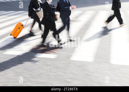 Bild mit Bewegungsunschärfe von japanischen Geschäftsleuten, die eine Stadtstraße auf einem Zebraübergang überqueren Stockfoto