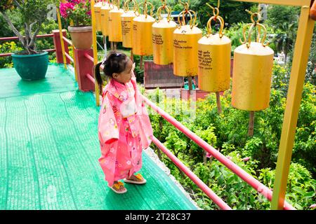 Thailändische Kinder Mädchen tragen Kimono traditionelle japanische Kleidung Reise Besuch und Metallglocke für Respekt betenden buddha des Wat Khao DIN Tempels in Supha Stockfoto