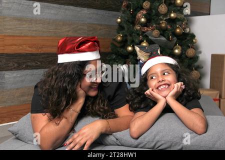 Die geschiedene alleinerziehende Mutter mit ihrer brünetten Latina-Tochter feiert Weihnachten neben dem geschmückten Baum in Einsamkeit Stockfoto