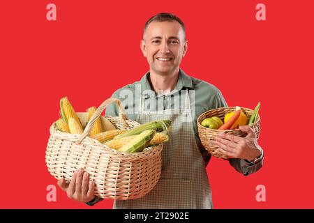 Reifer männlicher Bauer mit Korbkörben voller reifer Gemüse auf rotem Hintergrund Stockfoto