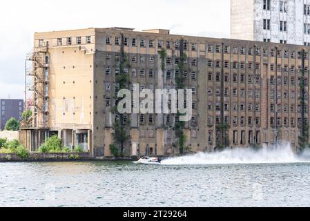 Stillgelegtes Rank Hovis Premier Mill-Lager am Royal Victoria Dock, Docklands, Newham, London, Großbritannien. 1904 gebaut, 1980 geschlossen Motorboot läuft vorbei Stockfoto