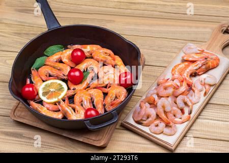 Garnelen mit Tigergarnelen, Tomaten und Zitrone in der Pfanne. Garnelen auf Schneidebrett. Heller Holzhintergrund. Gesunde appetitliche Nahrung. Draufsicht Stockfoto