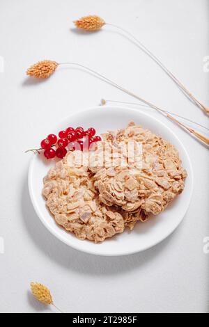 Vollkornkekse mit einem Zweig roter Johannisbeeren in einer kleinen weißen Platte, Seitenansicht Stockfoto