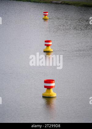 Rot-gelbe, weiße Bojen treiben in der Strömung auf der Wasseroberfläche eines Flusses Stockfoto