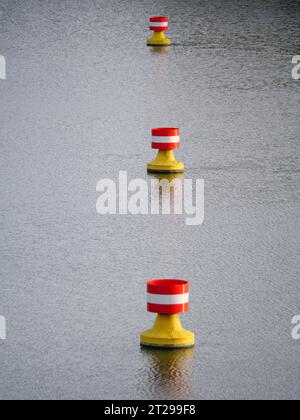 Rot-gelbe, weiße Bojen treiben in der Strömung auf der Wasseroberfläche eines Flusses Stockfoto