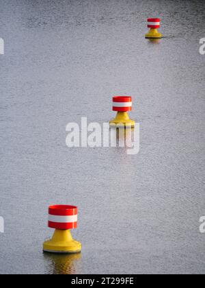 Rot-gelbe, weiße Bojen treiben in der Strömung auf der Wasseroberfläche eines Flusses Stockfoto