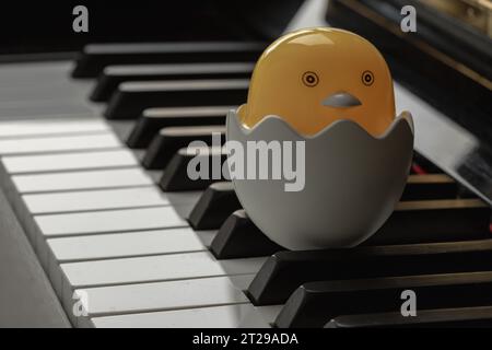 Baby-Chick-Zeichentrickfilm sitzt auf einem zerbrochenen Eierständer auf der Klaviertastatur. Gelbes süßes Huhn schlüpft aus Ei, Platz für Text, selektiver Fokus. Stockfoto