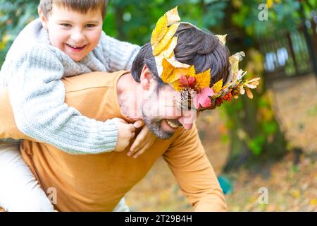 7. Oktober 2023: Vater und Sohn spielen im Herbst im Garten. Kleiner Junge auf dem Rücken seines Vaters mit einer herbstlich hausgemachten Krone aus bunten Blättern. Familie im Herbst Konzept *** Papa und Sohn spielen im Herbst im Garten. Kleiner Junge Huckepack auf dem Rücken von seinem Vater mit einer herbstlichen selbstgebastelten Krone aus bunten Blättern. Familie im Herbst Konzept Credit: Imago/Alamy Live News Stockfoto