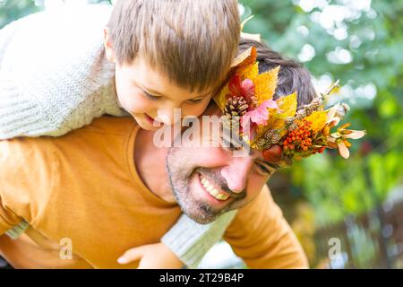 7. Oktober 2023: Vater und Sohn spielen im Herbst im Garten. Kleiner Junge auf dem Rücken seines Vaters mit einer herbstlich hausgemachten Krone aus bunten Blättern. Familie im Herbst Konzept *** Papa und Sohn spielen im Herbst im Garten. Kleiner Junge Huckepack auf dem Rücken von seinem Vater mit einer herbstlichen selbstgebastelten Krone aus bunten Blättern. Familie im Herbst Konzept Credit: Imago/Alamy Live News Stockfoto