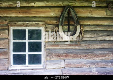 Ein altes Fenster in einer Holzwand und ein hängendes Pferdegeschirr Stockfoto