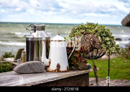Komposition mit Milchkännchen Teekanne und Stein auf Holztisch mit Meereshintergrund Stockfoto