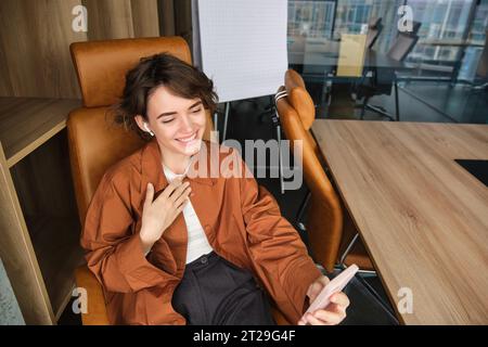 Porträt einer Frau, die Hallo sagt, mit dem Smartphone spricht, Video-Chats führt, ein Online-Meeting in ihrem Büro abhält, mit dem Mobiltelefon Gespräche führt Stockfoto