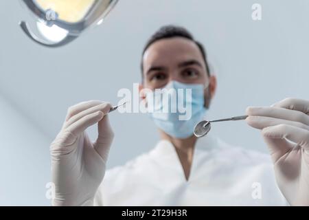 Niedriger Winkel Aufnahme eines männlichen Zahnarztes, Durchführung der Untersuchung und Überprüfung der Mundgesundheit, Zähne und Zahnfleisch des Patienten. Der Stomatologe hält Zahninstrumente Stockfoto
