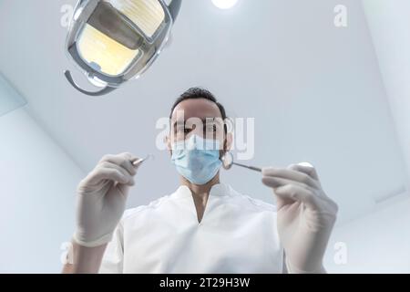 Niedriger Winkel Aufnahme eines männlichen Zahnarztes, Durchführung der Untersuchung und Überprüfung der Mundgesundheit, Zähne und Zahnfleisch des Patienten. Der Stomatologe hält Zahninstrumente Stockfoto