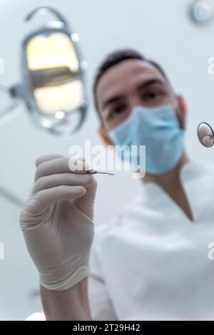 Niedriger Winkel Aufnahme eines männlichen Zahnarztes, Durchführung der Untersuchung und Überprüfung der Mundgesundheit, Zähne und Zahnfleisch des Patienten. Der Stomatologe hält Zahninstrumente Stockfoto