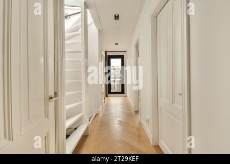 Langer schmaler Flur mit weißen Wänden und Türen, die zu verschiedenen Zimmern und Treppen in einem modernen Haus führen Stockfoto