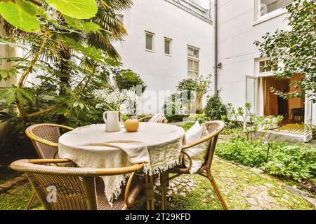 Esstisch und Stühle sind in einem kleinen Innenhof mit Pflanzen angeordnet, die außerhalb des Wohngebäudes wachsen Stockfoto