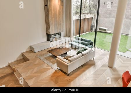 Blick auf das Wohnzimmer mit bequemen Sofas und Couchtisch vor dem Kamin und neben einem großen Fenster Stockfoto