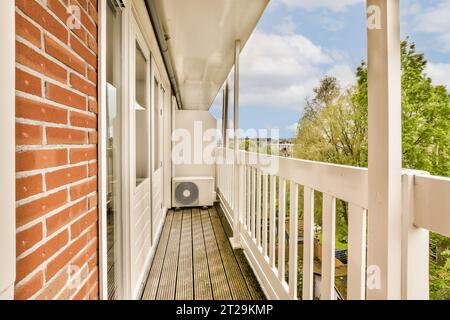 Leerer schmaler Balkon mit gemauerter Mauer und weißem Geländer gegen Bäume und bewölktem Himmel tagsüber Stockfoto
