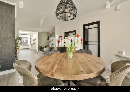 Die Leuchte hängt über einer Blumenvase auf einem hölzernen Esstisch, umgeben von leeren Stühlen in einem modernen Apartment Stockfoto