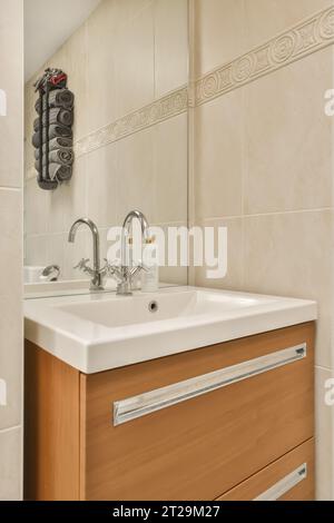 Spiegel über Keramikwaschbecken und Holzschrank mit Handtuchhalter an der gefliesten Wand im modernen Badezimmer zu Hause Stockfoto