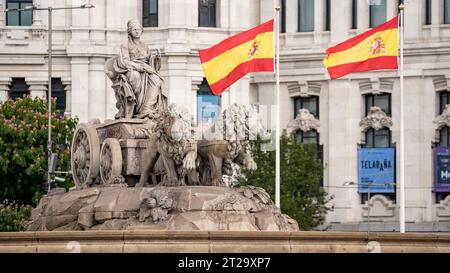 Madrid, Spanien; 16. 10. 2023: Statue auf der Plaza de Cibeles mit der Darstellung der gleichnamigen Göttin und zwei Löwen mit spanischer Flagge Stockfoto