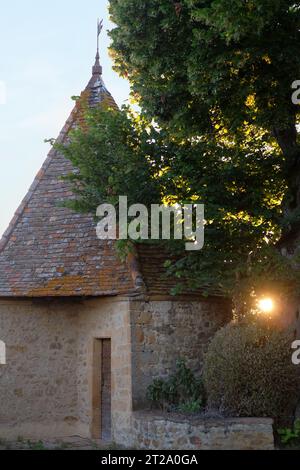 Ein kleiner mittelalterlicher Steinturm auf der Terrassenmauer von Chateau Bagnols, Frankreich, Sonnenuntergang, Licht durch Bäume, Blätter und Sträucher Stockfoto