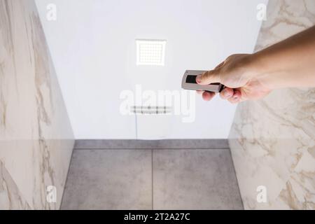 Ein Mann hält in der Hand eine Abluftsteuerung und eine Lichtsteuerung im Badezimmer. Stockfoto