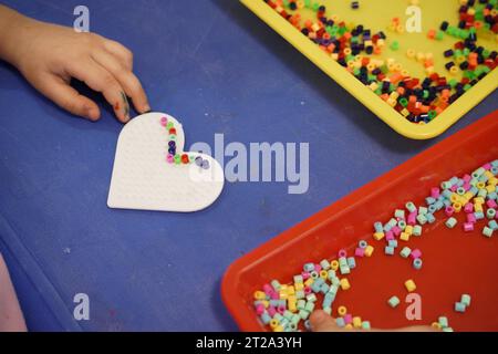 Perlen, Kinder, die Perlen basteln, ein Herz bunt Perlen basteln. Stockfoto