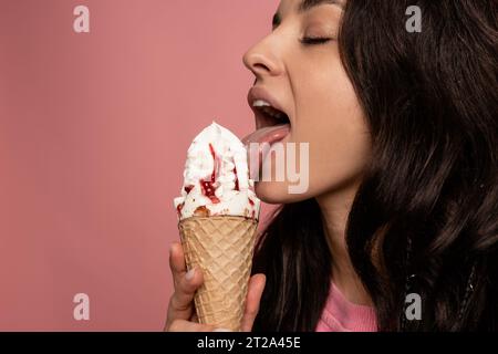 Junge dunkelhaarige Frau genießt einen köstlichen Eisbecher mit geschlossenen Augen während des Fotoshootings im Studio. Konzept für den Genuss von Süßspeisen Stockfoto