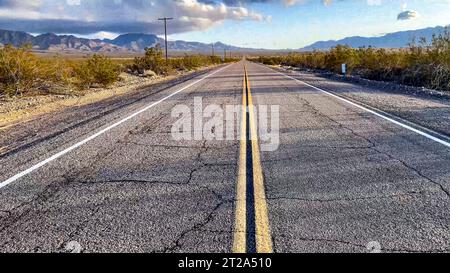 Die gelbe Linie setzt eine Straßenmarkierung auf dem Asphalt eines endlosen Highway an der US Route 66 fort, der die Mojave-Wüste durchquert. Stockfoto