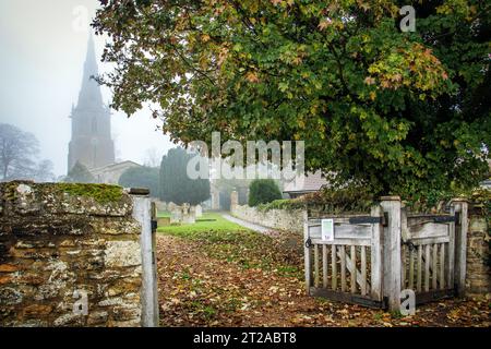 Im Herbst, im Dorf Sharnbrook, Bedfordshire, England, schaute man durch ein Tor in Richtung St. Peter's Pfarrkirche, die in Nebel gehüllt war Stockfoto