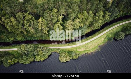 Aus der Vogelperspektive auf einen gewundenen Pfad durch einen grünen Wald entlang eines ruhigen Flusses Stockfoto