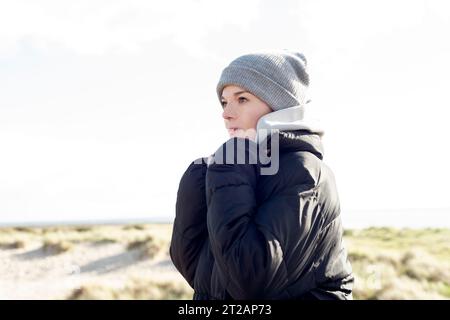 Porträt einer Frau mit Wollmütze und Mantel, die am Strand läuft. Trainingskonzept im Winter. Stockfoto