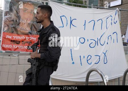 Ein bewaffneter Polizist steht neben einem Schild mit der Aufschrift "jetzt die Geiseln freilassen" während eines Protests von Familienmitgliedern israelischer Geiseln, die letzte Woche von der militanten palästinensischen Gruppe Hamas geschnappt wurden, Wache. außerhalb der Militärbasis HaKirya, die am 16. Oktober 2023 das Hauptquartier des israelischen Verteidigungsministeriums und Büros des IDF-Generalstabs in Tel Aviv, Israel, beherbergt. Stockfoto