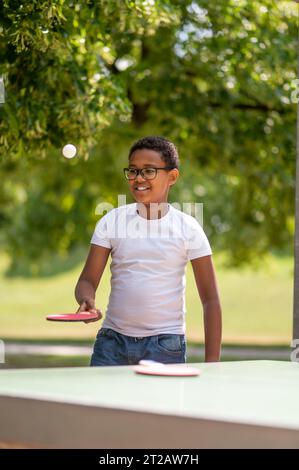 Ein Junge in einem weißen T-Shirt, der Tischtennis spielt Stockfoto