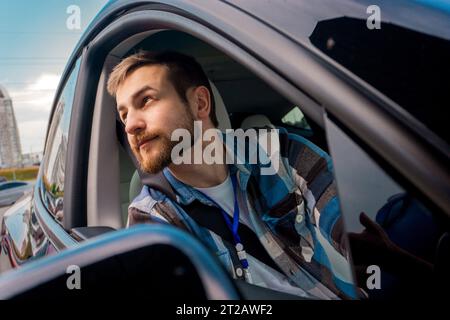 Junger bärtiger Passagier, der aus dem Fenster eines Autos blickt. Reise, Lifestyle, Verkehrskonzept Stockfoto