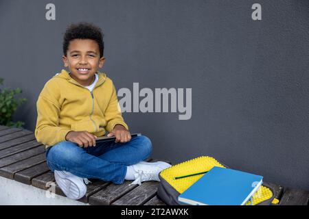 Lächelnder, lockiger Junge in gelbem Hoodie, der auf der Holzbank sitzt Stockfoto